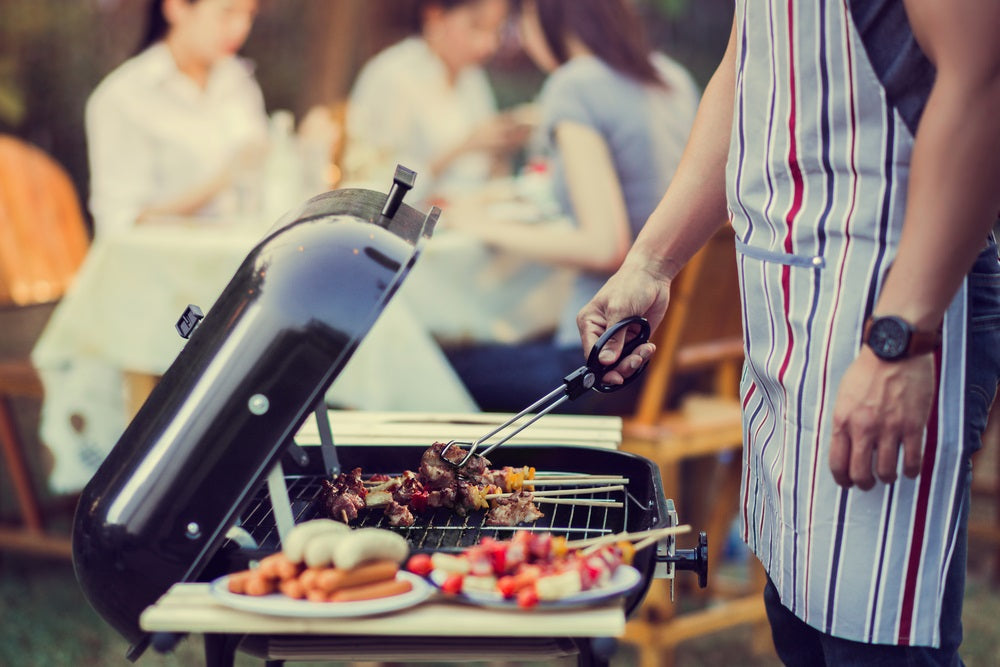 Outdoor catering barbecue man turning kebabs on a folding barbecue